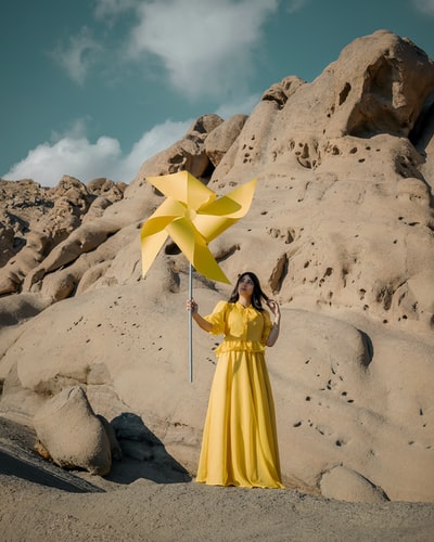 白天站在白色沙滩上的穿黄色衣服的女人